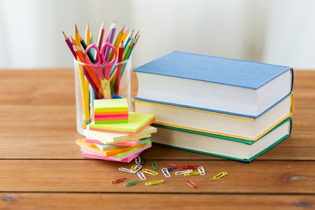 Education school supplies and object concept close up of stand or glass with writing tools and book with scissors on wooden table